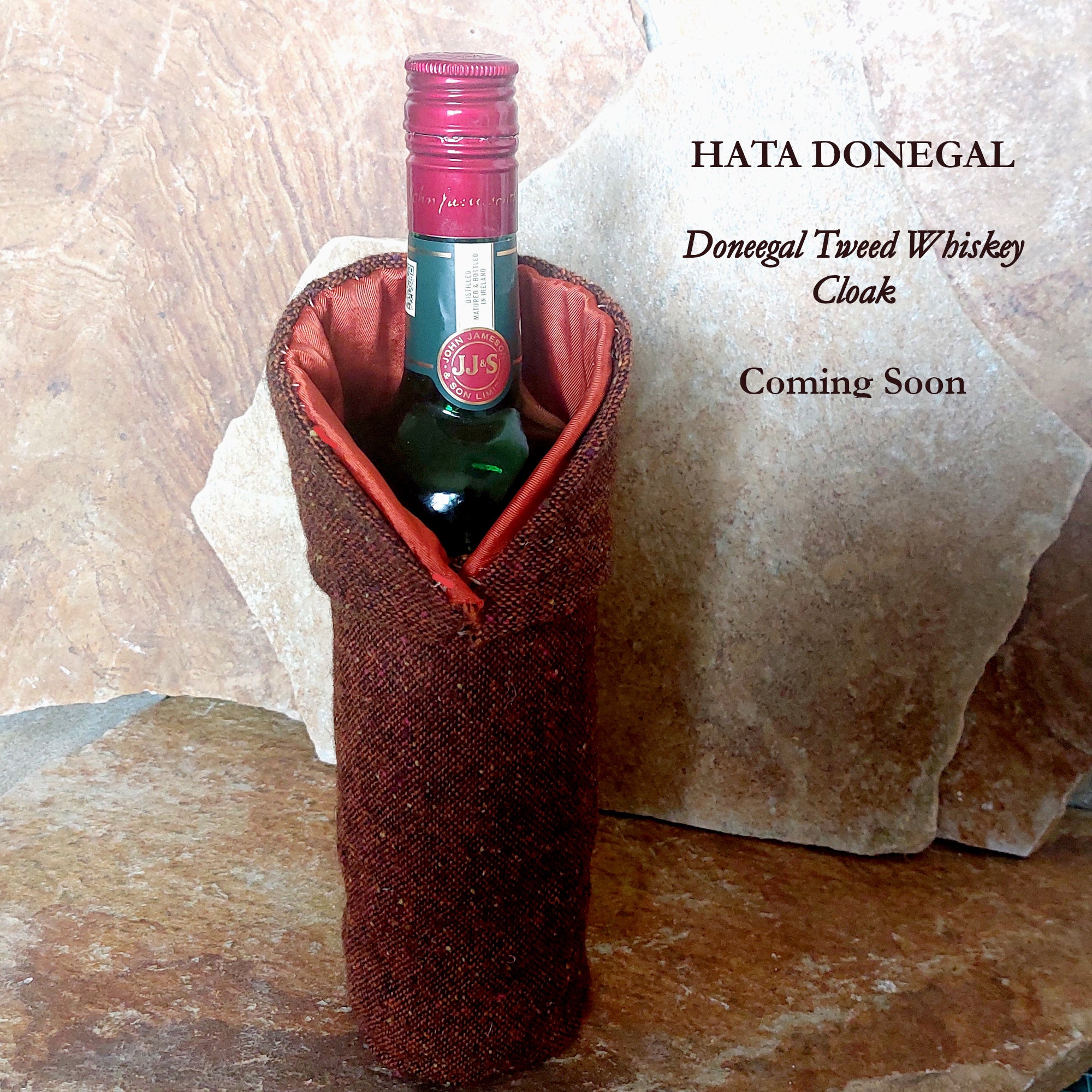 Donegal Tweed Whiskey Cloak viewed from the side with asymmetrical monk-style collar wrapped around a whiskey bottle against Donegal stone background.