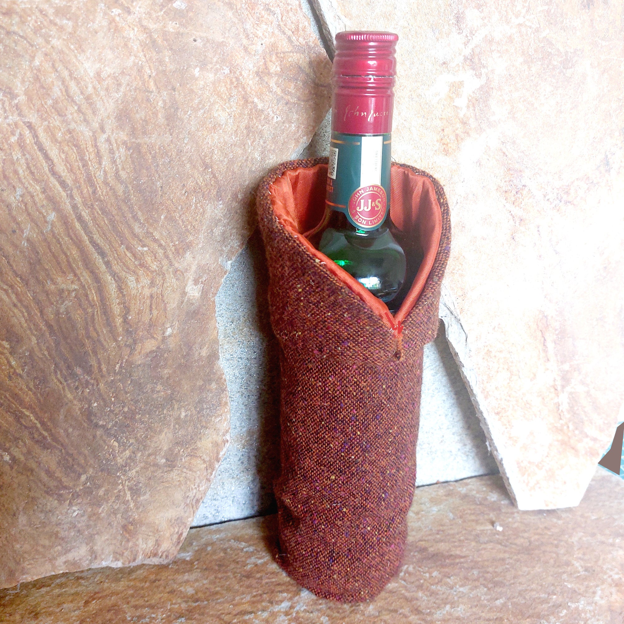 Donegal Tweed Whiskey Cloak viewed from the side with asymmetrical monk-style collar wrapped around a whiskey bottle against Donegal stone background.
